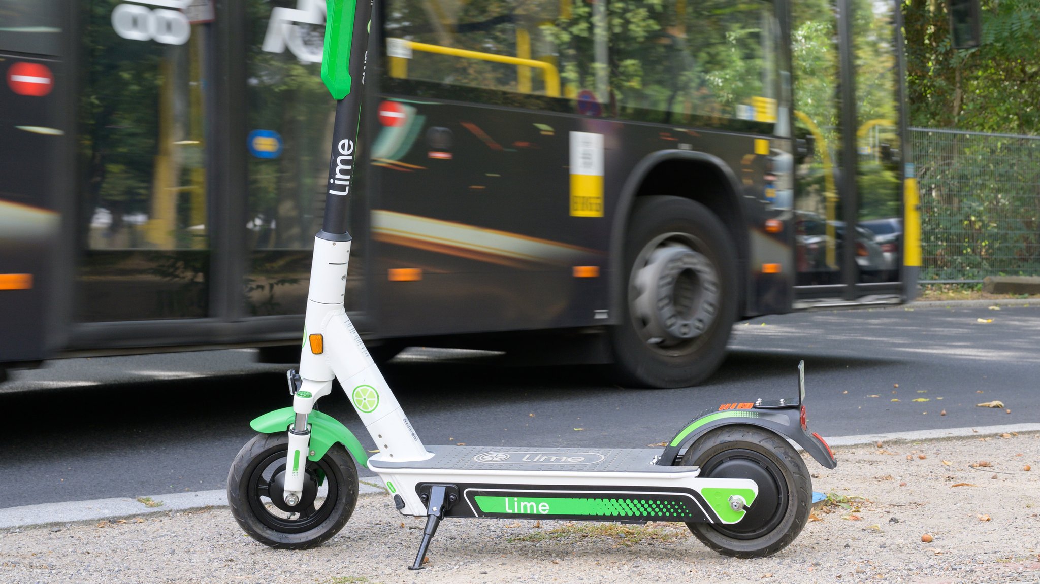 Ein E-Scooter steht auf einem Gehweg. Im Hintergrund fährt ein Bus vorbei. 