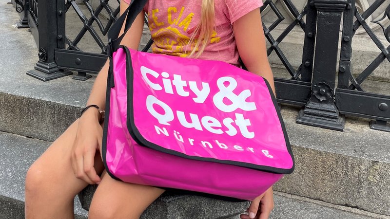 "City&Quest" nennt sich die neue Rätsel-Tour durch Nürnberg. Die Aufschrift ist groß auf die pinkfarbige Rätseltasche gedruckt.