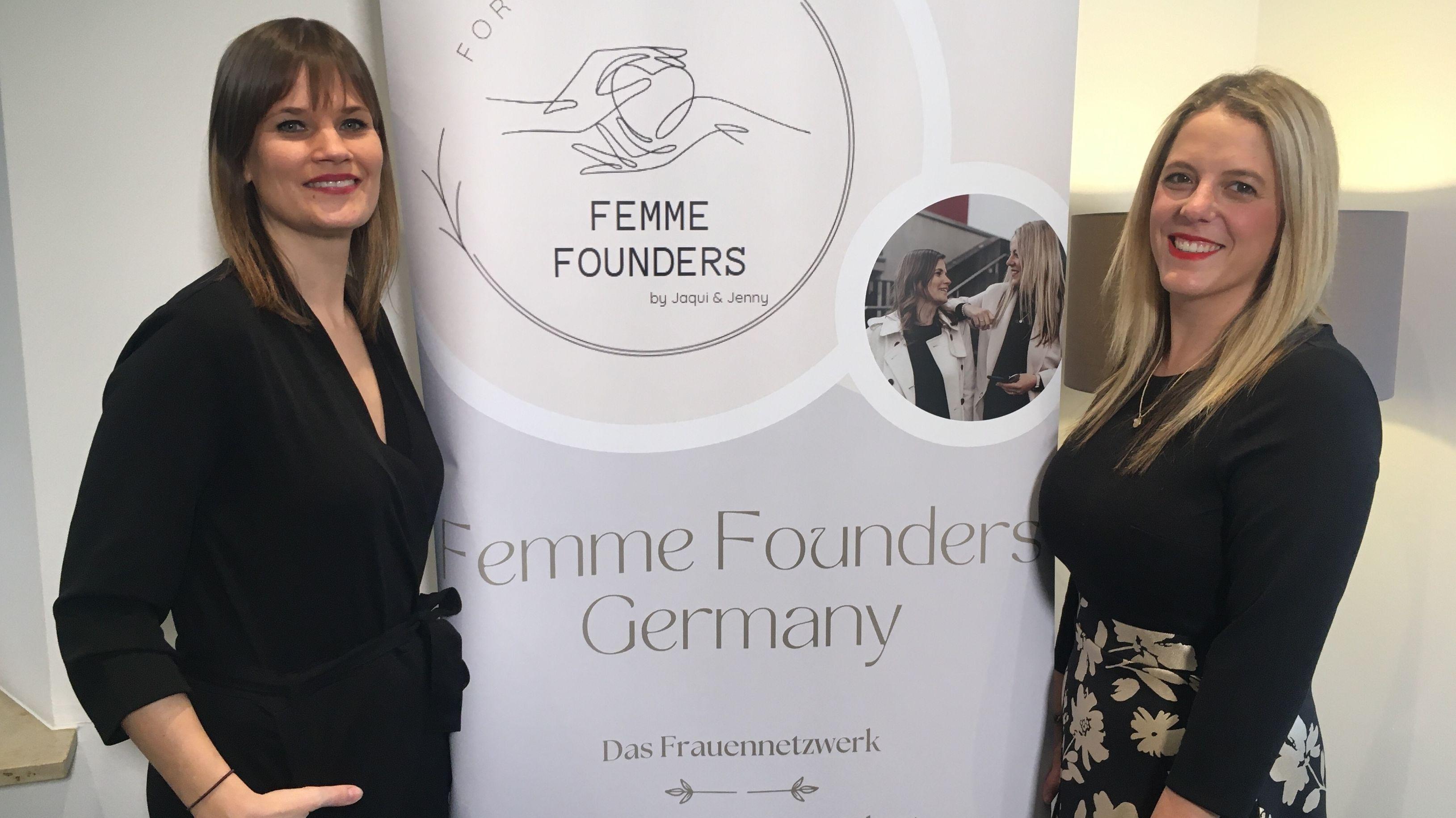 Zwei Frauen stehen grinsend vor einem Plakat der "Femme Founders Germany". 