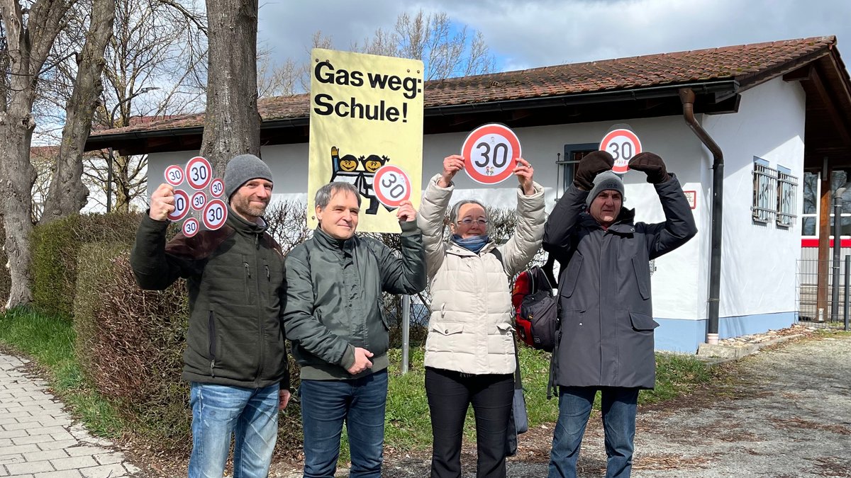 v.l.: Christian Guse, Michael Behrens, Eva Guse und Hans Aigner halten selbstgebastelte Tempo-30-Schilder hoch. Im Hintergrund ist ein Schild zu sehen, auf dem "Gas weg: Schule!" steht. 