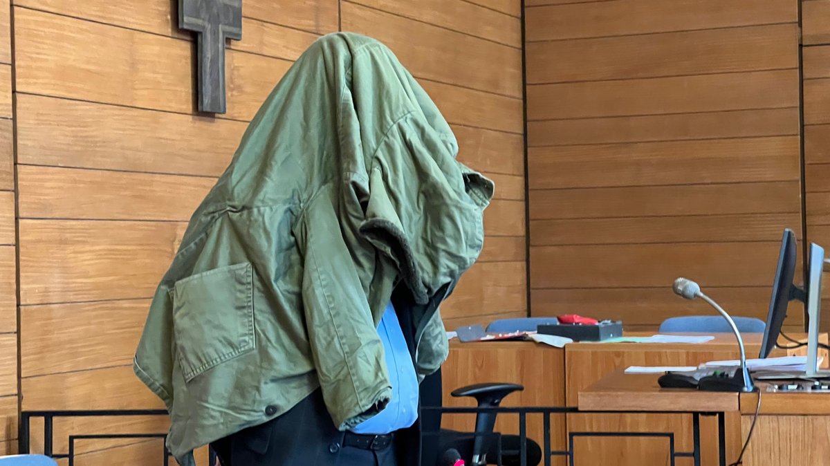 Ein Mann steht mit einer Jacke über dem Kopf im Gerichtssaal.
