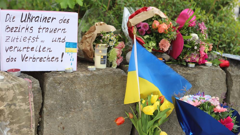 28.04.2024, Bayern, Murnau: Am Gelände eines Einkaufszentrums, an dem am Samstagabend (27.04.2024) zwei Männer aus der Ukraine getötet worden sind, wurden Blumen niedergelegt, sowie eine kleine ukrainische Flagge aufgestellt. Die Polizei konnte einen Mann festnehmen, der als dringend tatverdächtig gilt. Es handelt sich dabei um einen 57 Jahre alten Russen. Foto: Constanze Wilz/dpa +++ dpa-Bildfunk +++ | Bild:dpa-Bildfunk/Constanze Wilz