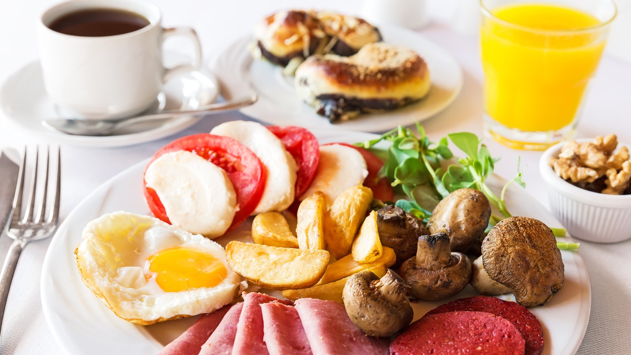 Ein reichhaltig gedeckter Tisch mit Kaffee, Croissants, Orangensaft und ein einen Teller mit Wurstaufschnitt, Pilzen, Tomaten-Mozarella-Salat, Champignons und Spiegeleiern.