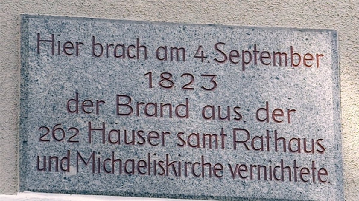 Ein Gedenktafel an einem Haus weist in roter Schrift daraufhin, dass hier am 4. September 1823 ein Feuer 262 Häuser, das Rathaus und die Michaeliskirche zerstörte. 