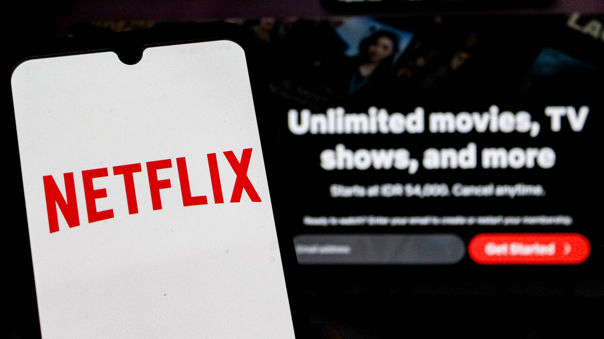 Das Netflix-Logo erscheint auf einem Handy-Bildschirm, dahinter läuft Netflix auf einem Fernsehgerät.