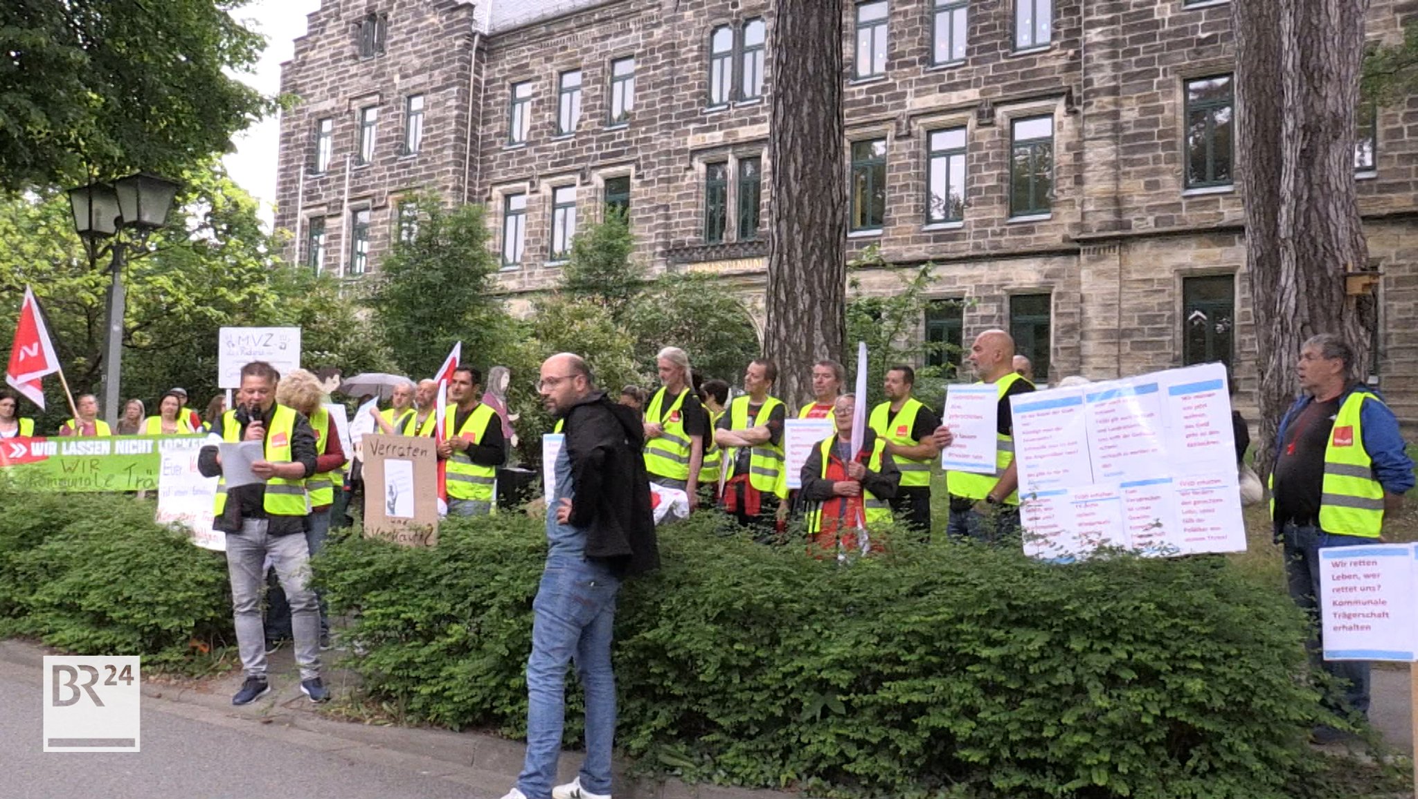 Demonstranten Protestieren vor einem Gebäude mit Fahnen und Spruchbändern. 