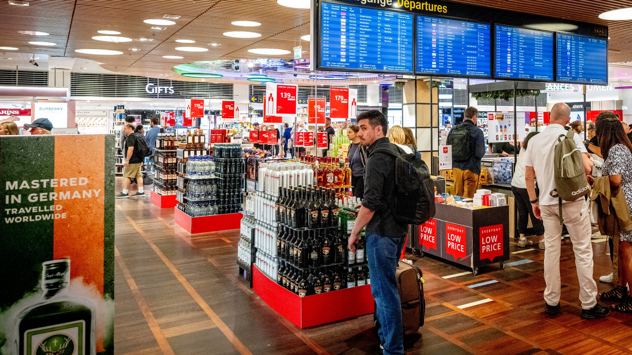 Verschiedene Flaschen mit alkoholischen Getränken werden in einem Duty-Free-Shop angeboten. Flugpassagiere betrachten die Waren.