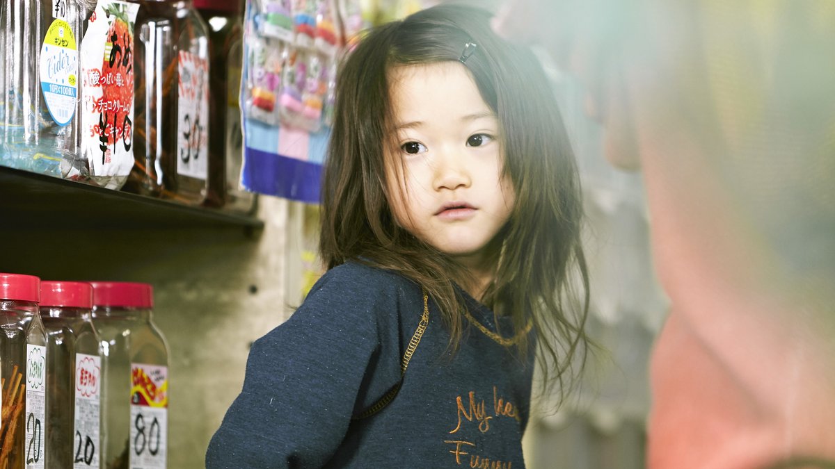 Ein kleines japanisches Mädchen steht vor einem Ladenregal - Szene aus "Shoplifters"