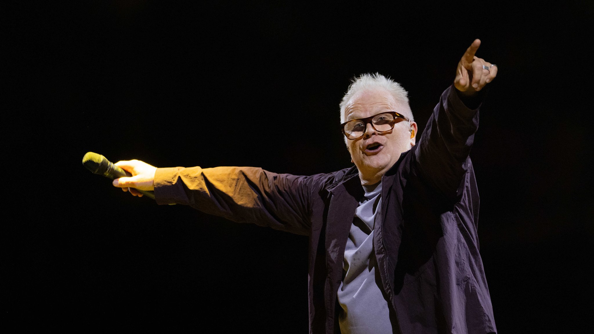 Herbert Grönemeyer in lässiger Kleidung, mit weit ausgebreiteten Armen und Mikro in der Hand