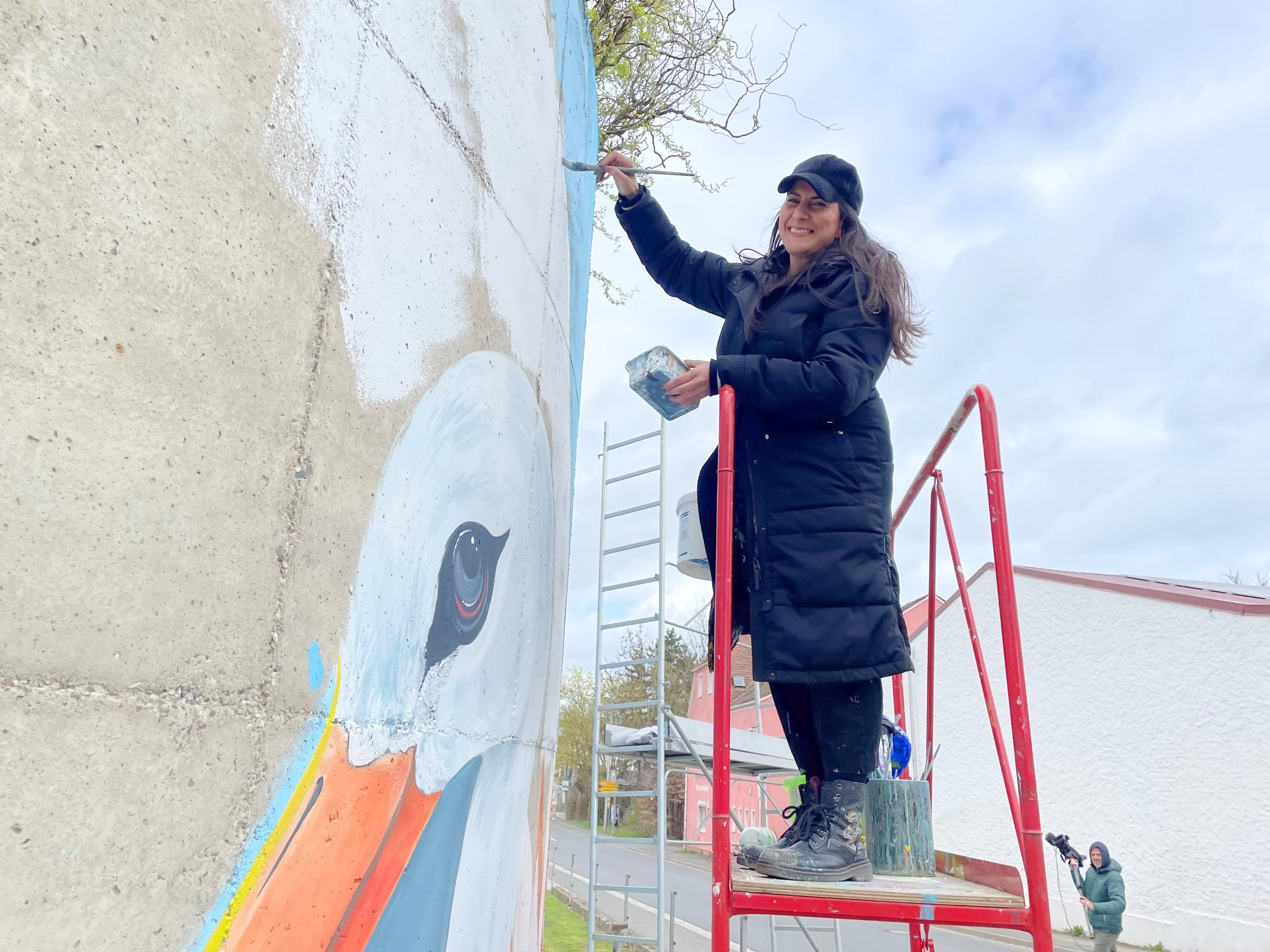 Die Küstlerin Liliana Martinez steht auf einer Leiter und bemalt einen Silo.
