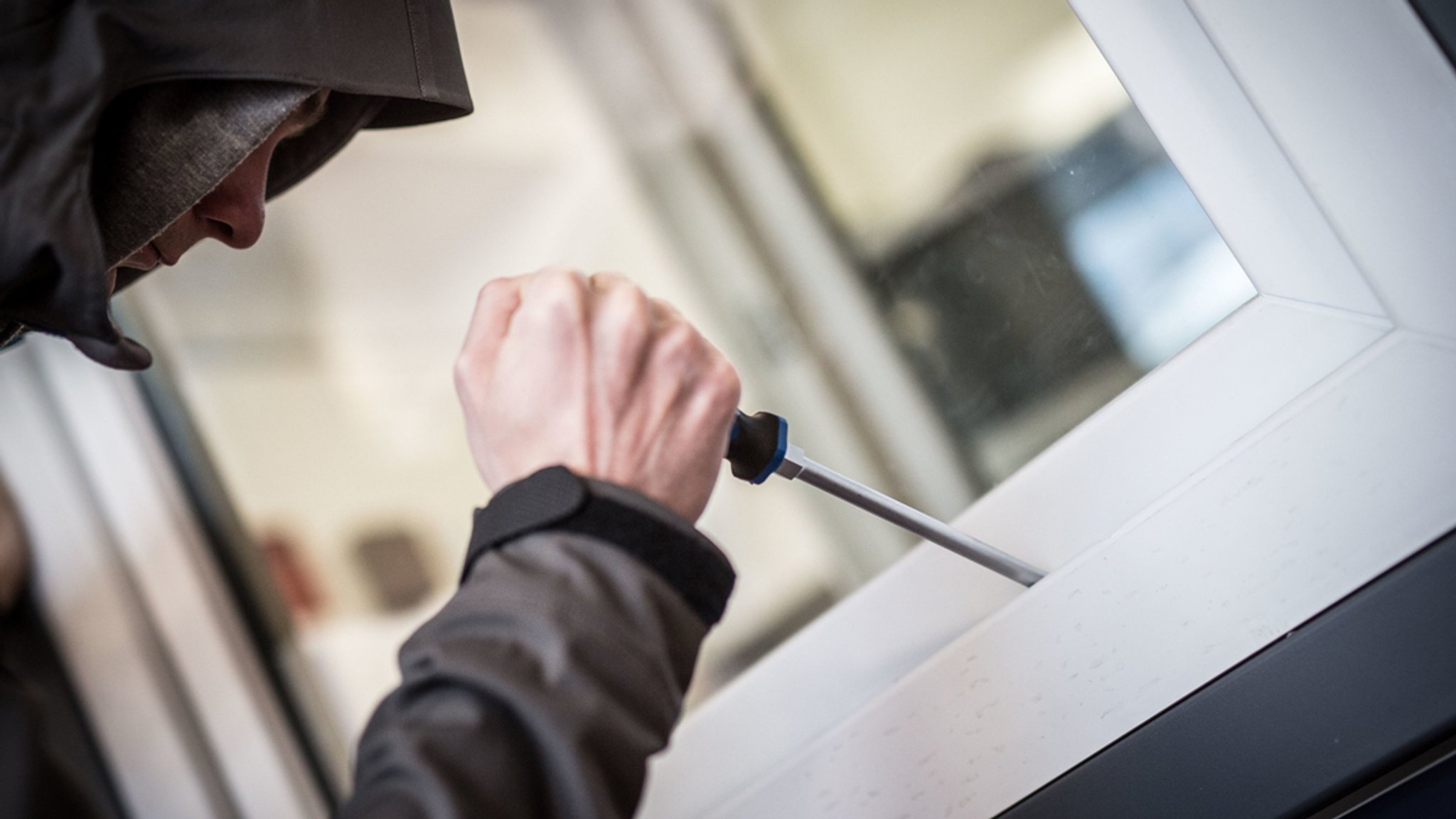 Ein Mann hebelt ein Fenster auf