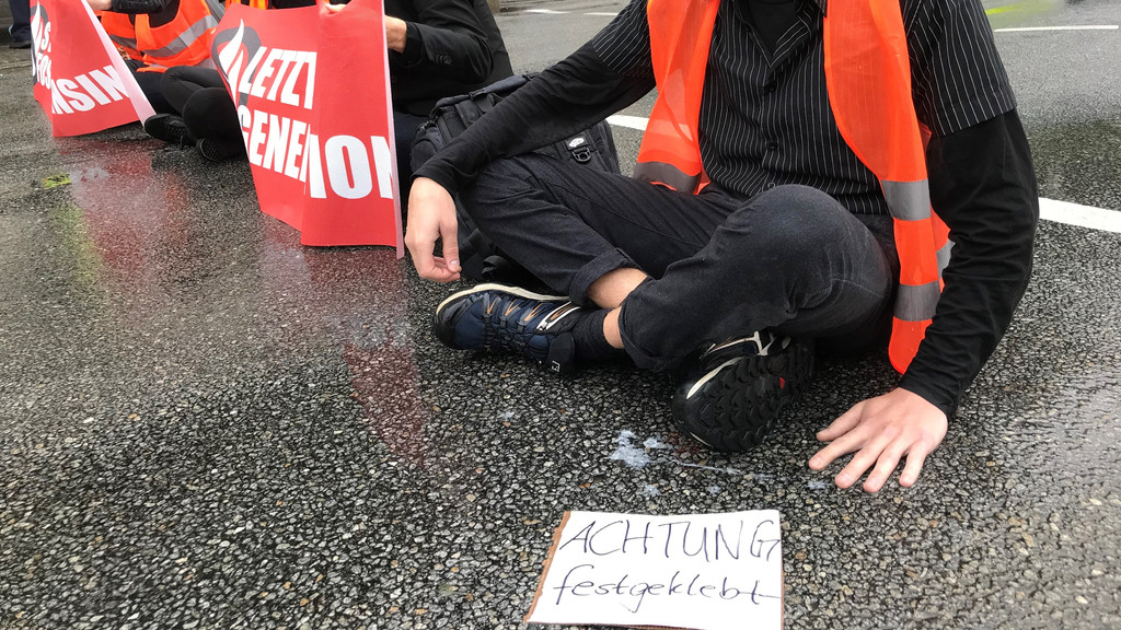 Die Aktivisten sitzen auf der Straße mit einem Zettel: "Achtung festgeklebt"