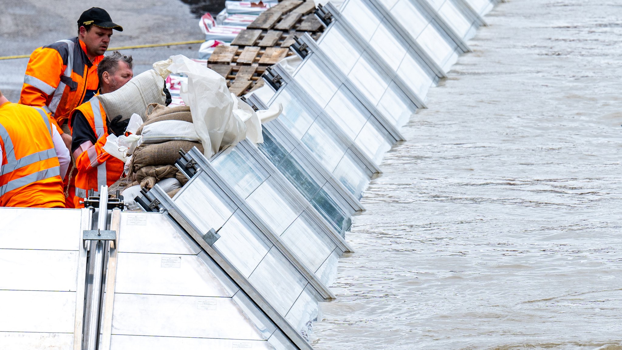 Helfer arbeiten an Schutzwänden am Donauufer in Regensburg