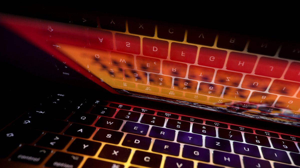 Symbolbild eines halb zugeklappten Laptops in Nahaufnahme. Aus dem Bildschirm leuchtet es orange.