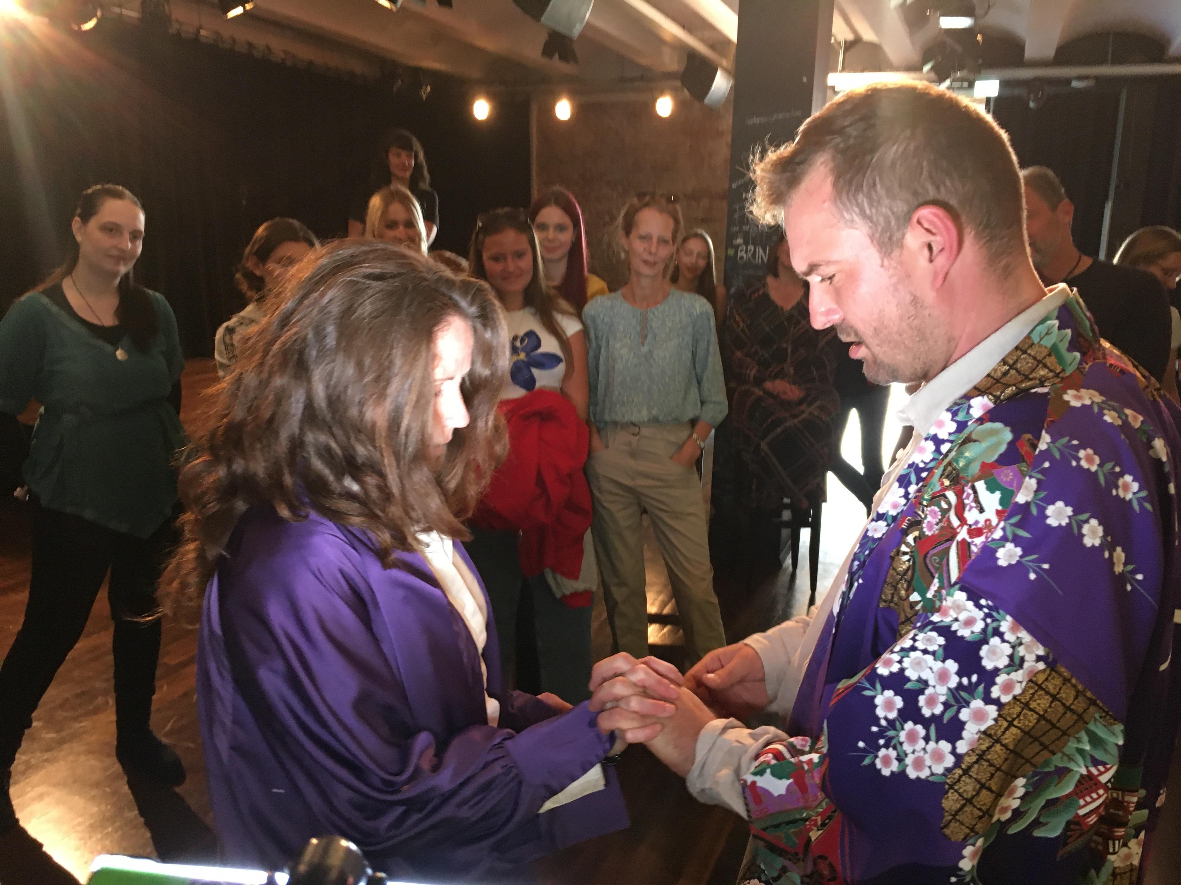 Zwei Schauspieler halten sich an den Händen, das Publikum schaut zu.