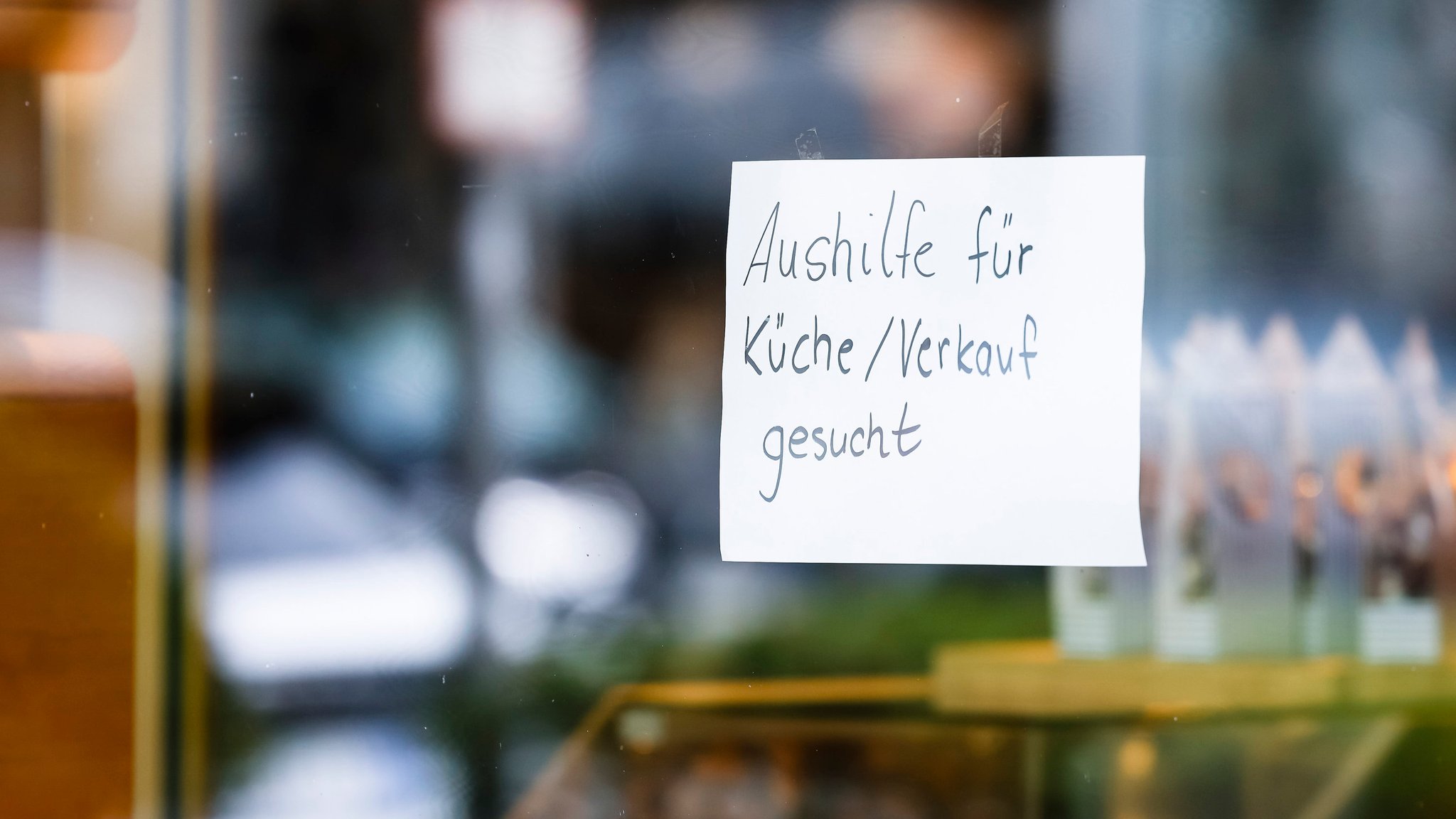 Ein Zettel mit der Aufschrift "Aushilfe für Küche/Verkauf gesucht" hängt an der Scheibe einer Konditorei (Symbolbild).