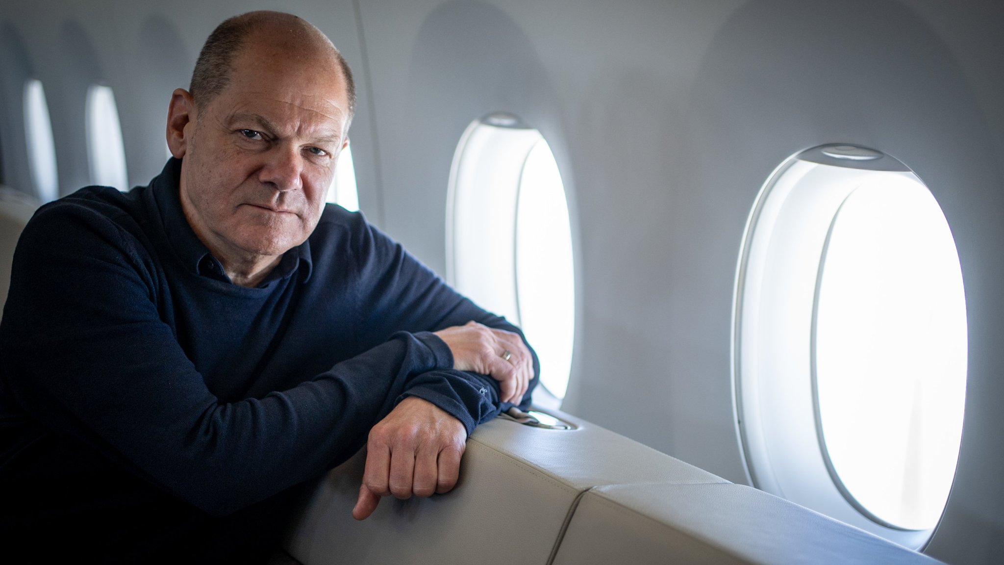 Kanzler Olaf Scholz blickt im Airbus A350 der Luftwaffe auf dem Rückweg von Tokio in die Kamera des Fotografen. 