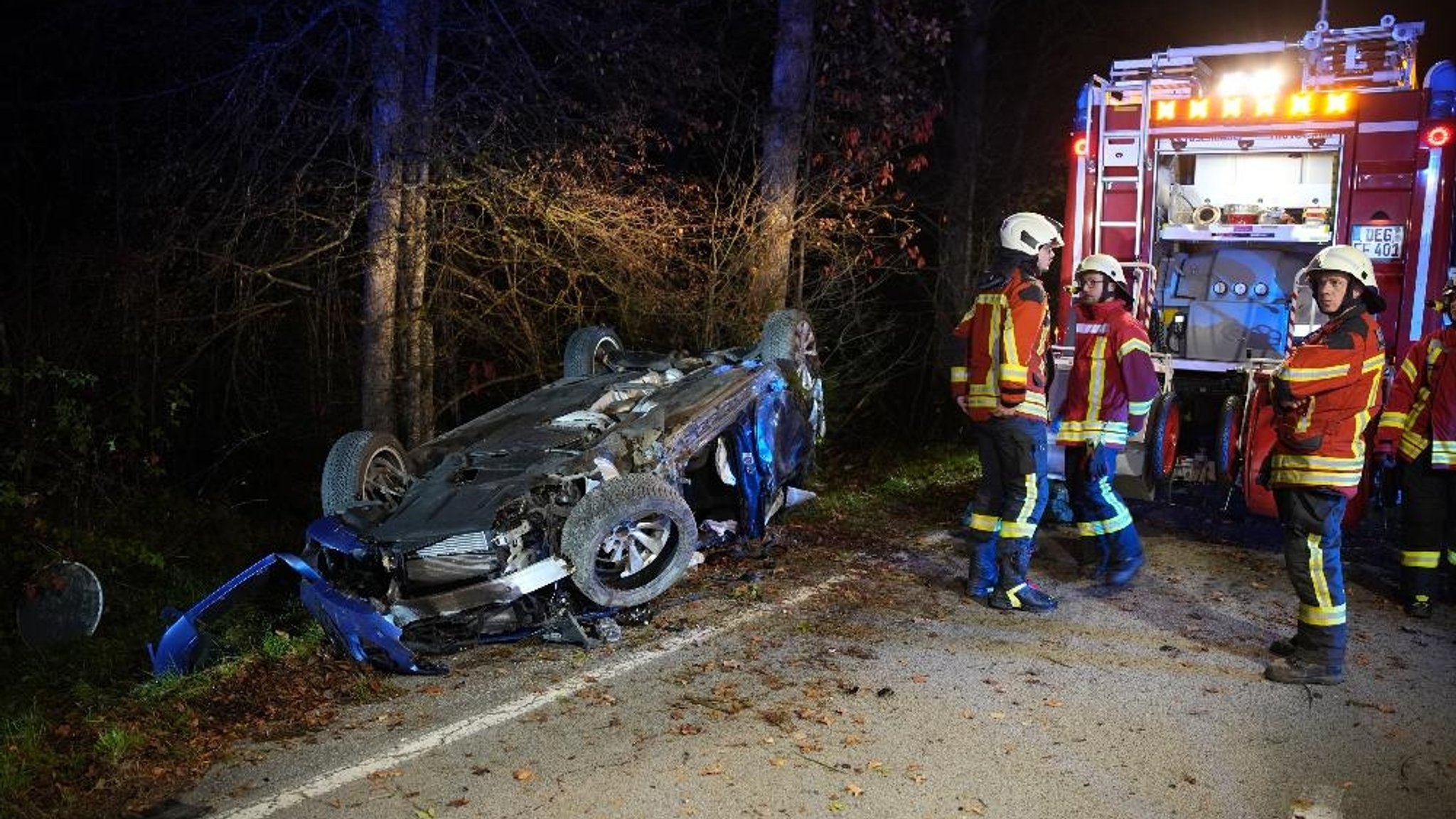 Feuerwehrmänner neben einem Autowrack im Wald. 