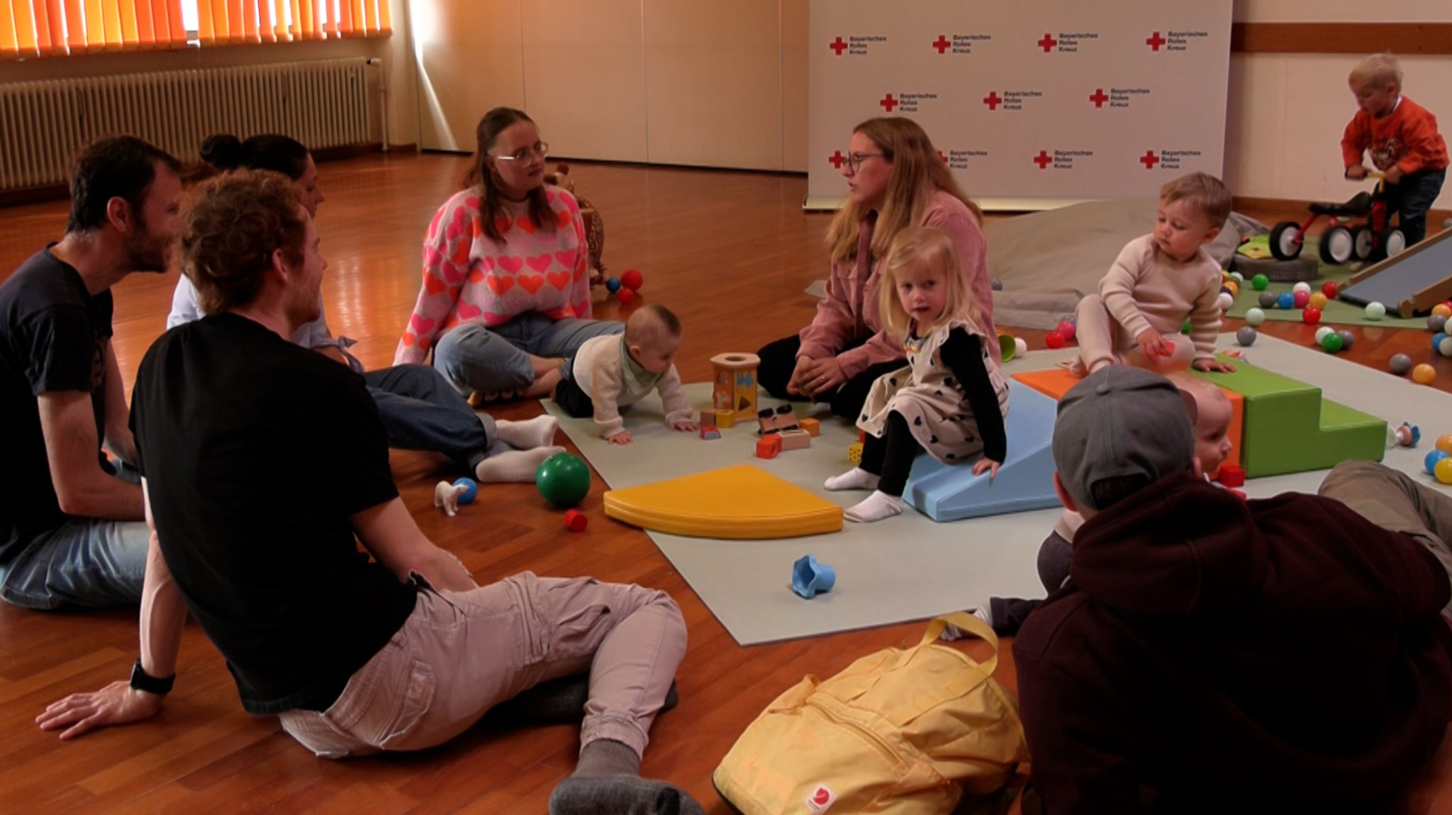 Erwachsene und Kinder sitzen auf einem Boden im Kreis und unterhalten sich. | Bild: BR/Vera Held Erwachsene und Kinder sitzen auf einem Boden im Kreis und unterhalten sich.