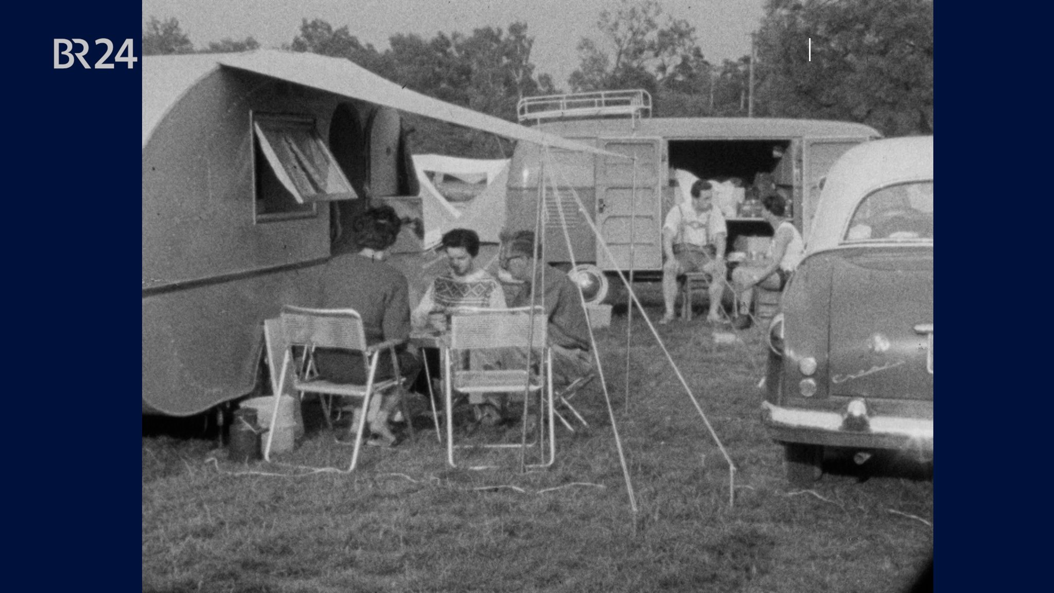 Autos und Wohnwagen auf einem Campingplatz, Menschen sitzen auf Campingmöbeln