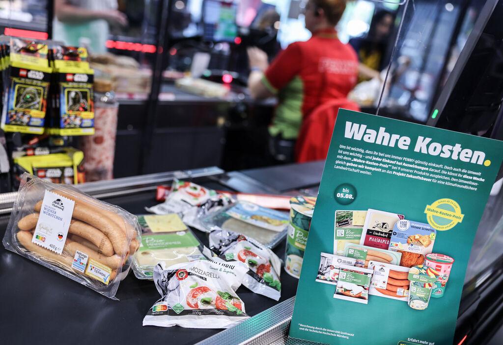 ARCHIV - 26.07.2023, Nordrhein-Westfalen, Köln: Produkte deren Preis mit den verdeckte Kosten angepasst wurden, liegen an der Kasse. Bei der «Wahre-Kosten-Aktion» des Discounters Penny sind die Verkaufszahlen nicht so stark gesunken wie erwartet. (zu dpa "Pennys «Wahre Kosten»: Verkäufe weniger stark gesunken als erwartet") Foto: Oliver Berg/dpa +++ dpa-Bildfunk +++