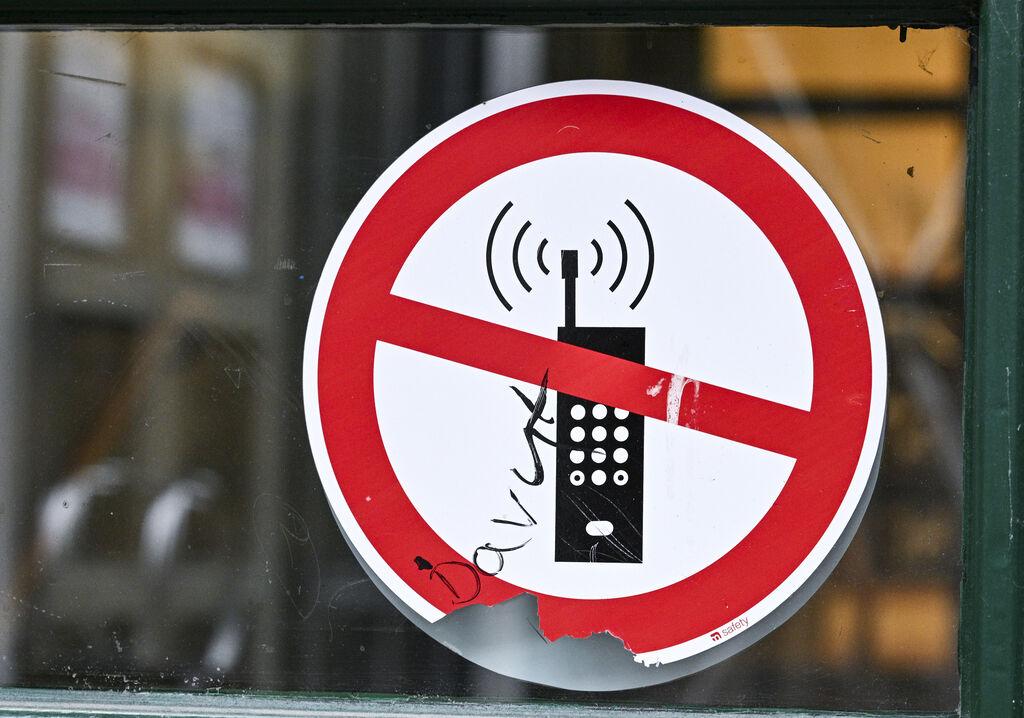 (Symbolbild) Ein Schild mit einem durchgestrichenen Handy-Symbol weist in einer Schule auf das Handyverbot hin.