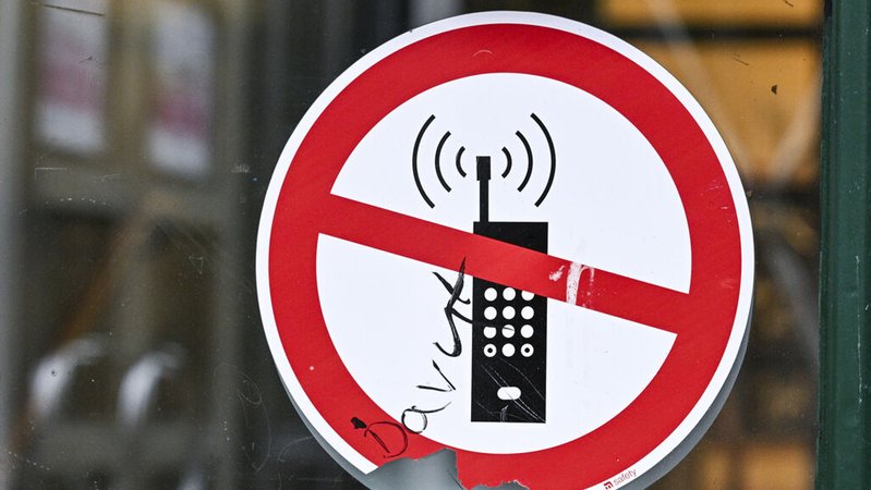 (Symbolbild) Ein Schild mit einem durchgestrichenen Handy-Symbol weist in einer Schule auf das Handyverbot hin. | Bild: dpa-Bildfunk/Jens Kalaene (Symbolbild) Ein Schild mit einem durchgestrichenen Handy-Symbol weist in einer Schule auf das Handyverbot hin.