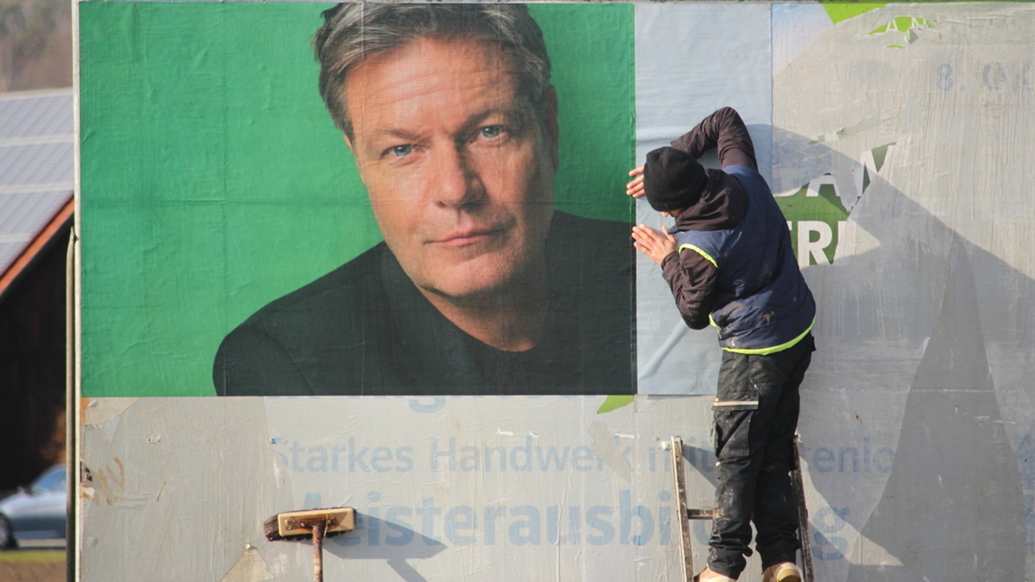 Ein Mann klebt ein Wahlplakat der Grünen an eine Plakatwand.