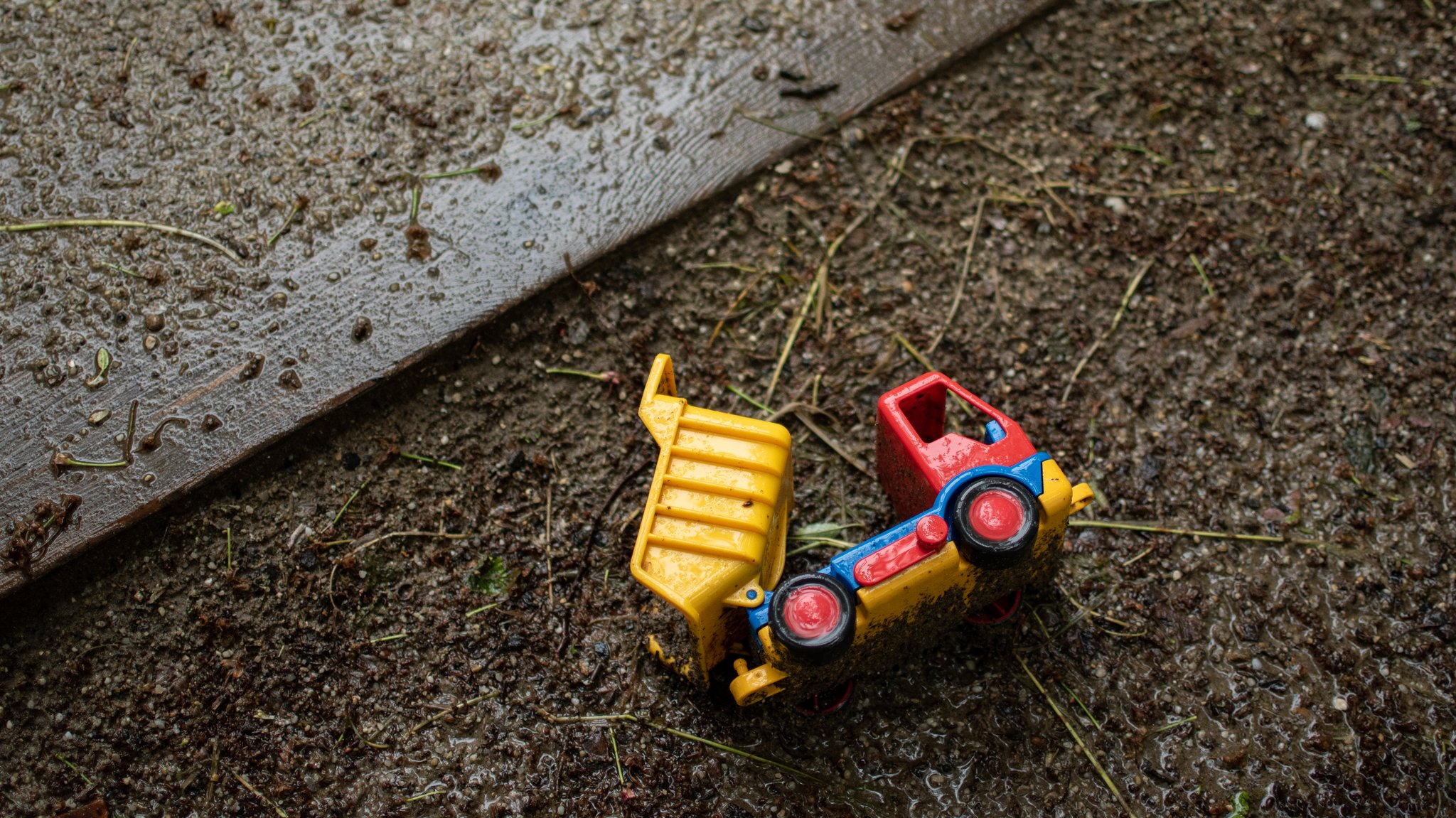 Ein Plastik LKW liegt am Sandkasten im Regen.