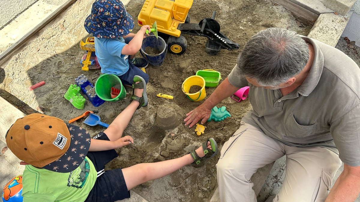 Ein Vater spielt mit seinen beiden Söhnen im Sandkasten. 