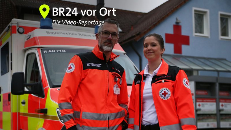 Ein Notfallsanitäter und eine Rettungssanitäterin stehen in Arbeitskleidung vor einem Rettungswagen. | Bild: BR \ Isabel Pogner Ein Notfallsanitäter und eine Rettungssanitäterin stehen in Arbeitskleidung vor einem Rettungswagen.