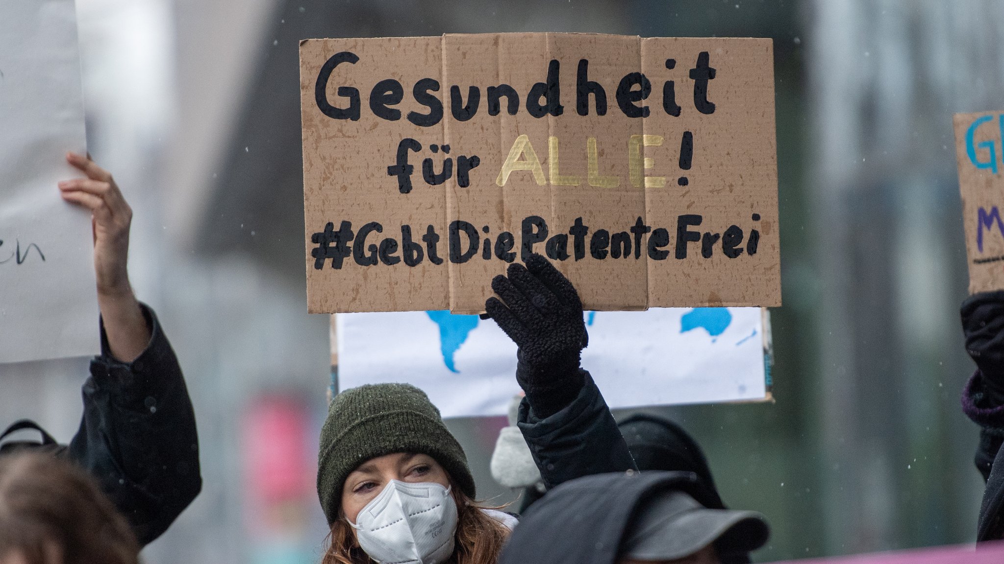 Teilnehmerin einer Demonstration hält ein Plakat, auf dem die Patentfreigabe von Corona-Impfstoffen gefordert wird.