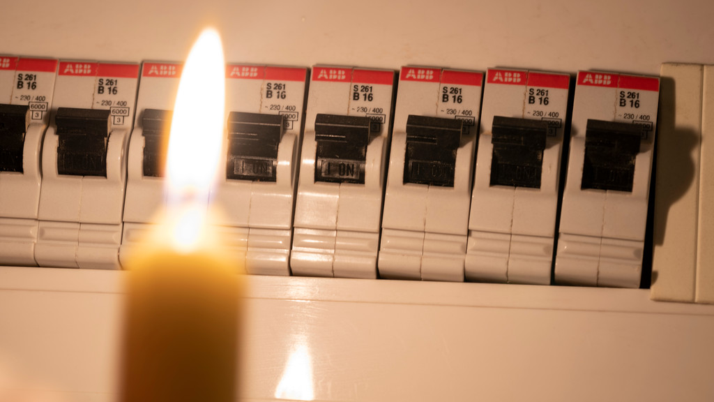 Eine brennende Kerze vor einem Sicherungskasten (Symbolbild)
