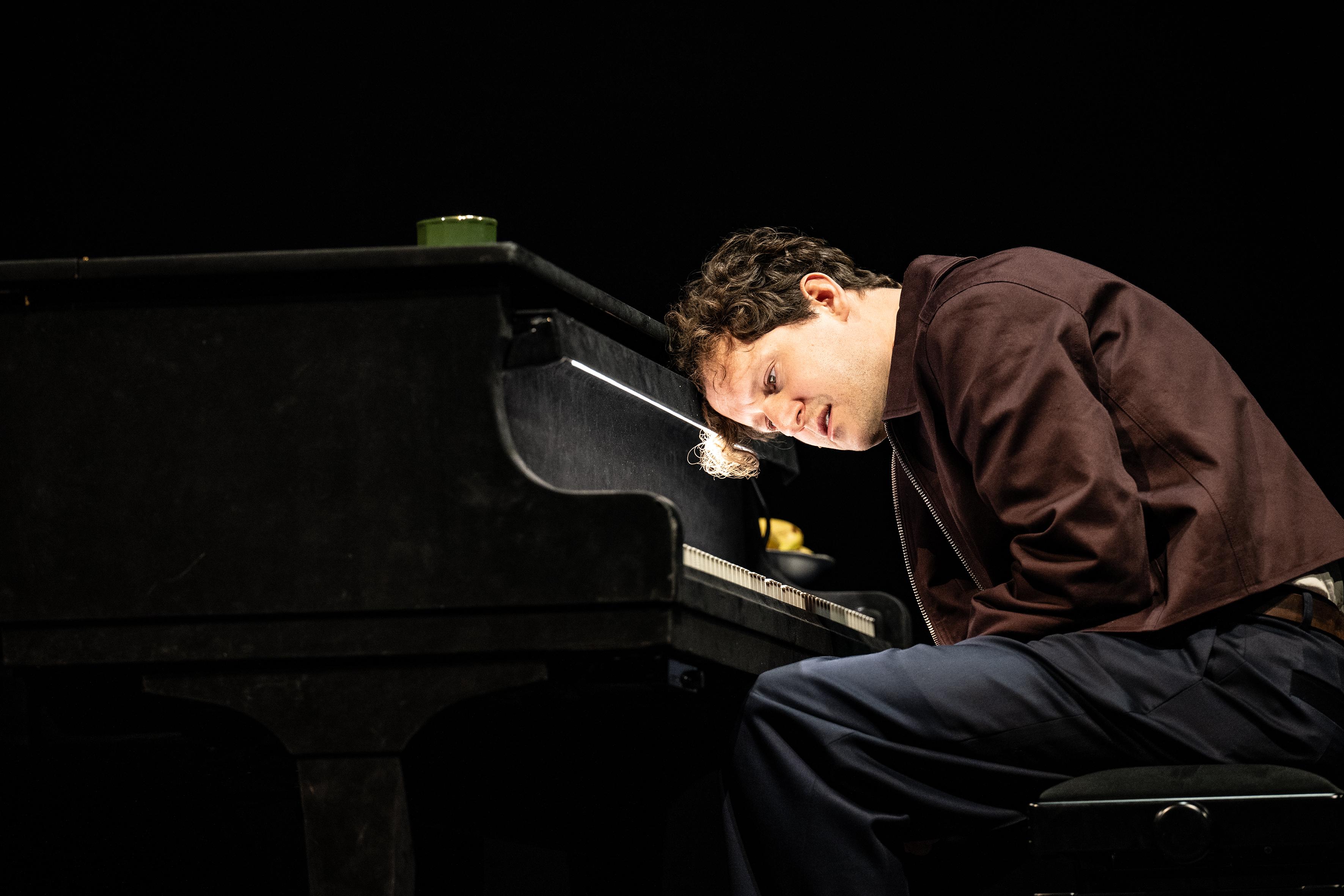 Schauspieler Moritz Treuenfels sitzt an einem Klavier und beugt sich über die Tastatur, er trägt eine braun glänzende Jacke.