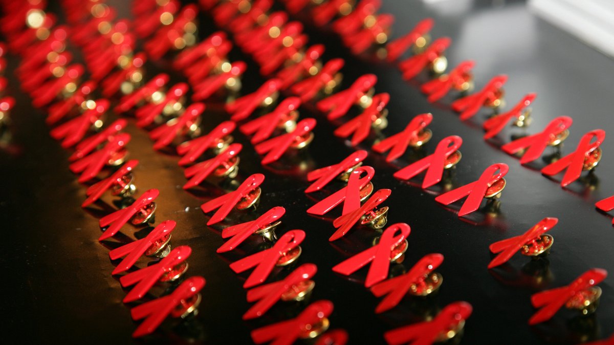 Rote Aids-Schleifen als Anstecker liegen auf einem Tisch.