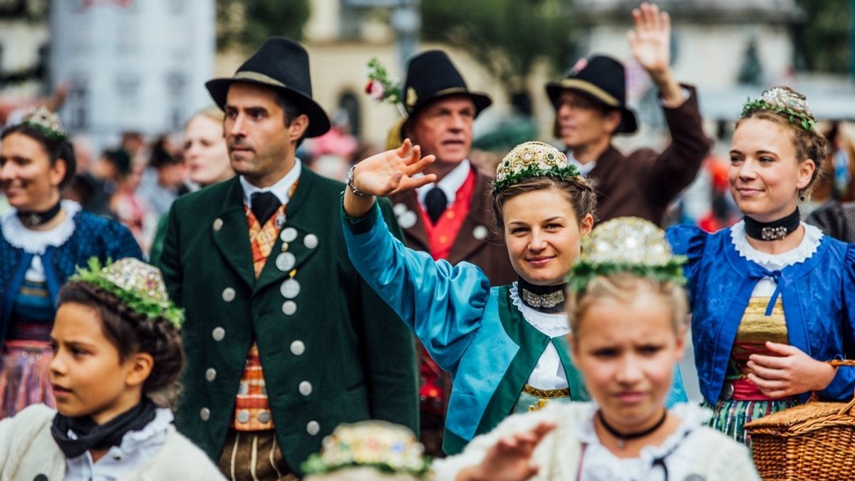 Frauen, Männer und Kinder in historischer Tracht laufen lächelnd und winkend durch die Münchner Straßen