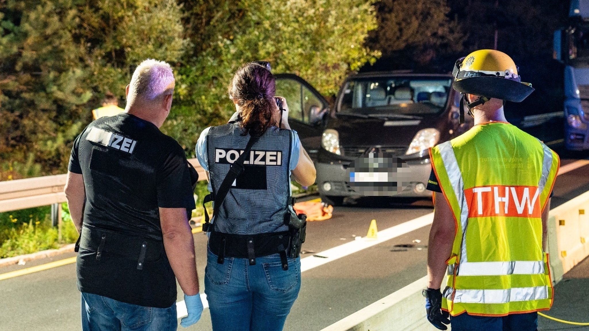 Polizeibeamte und ein Mitarbeiter des THW stehen auf der Autobahn vor einem Transporter. Davor liegen Gegenstände auf der Fahrbahn. 