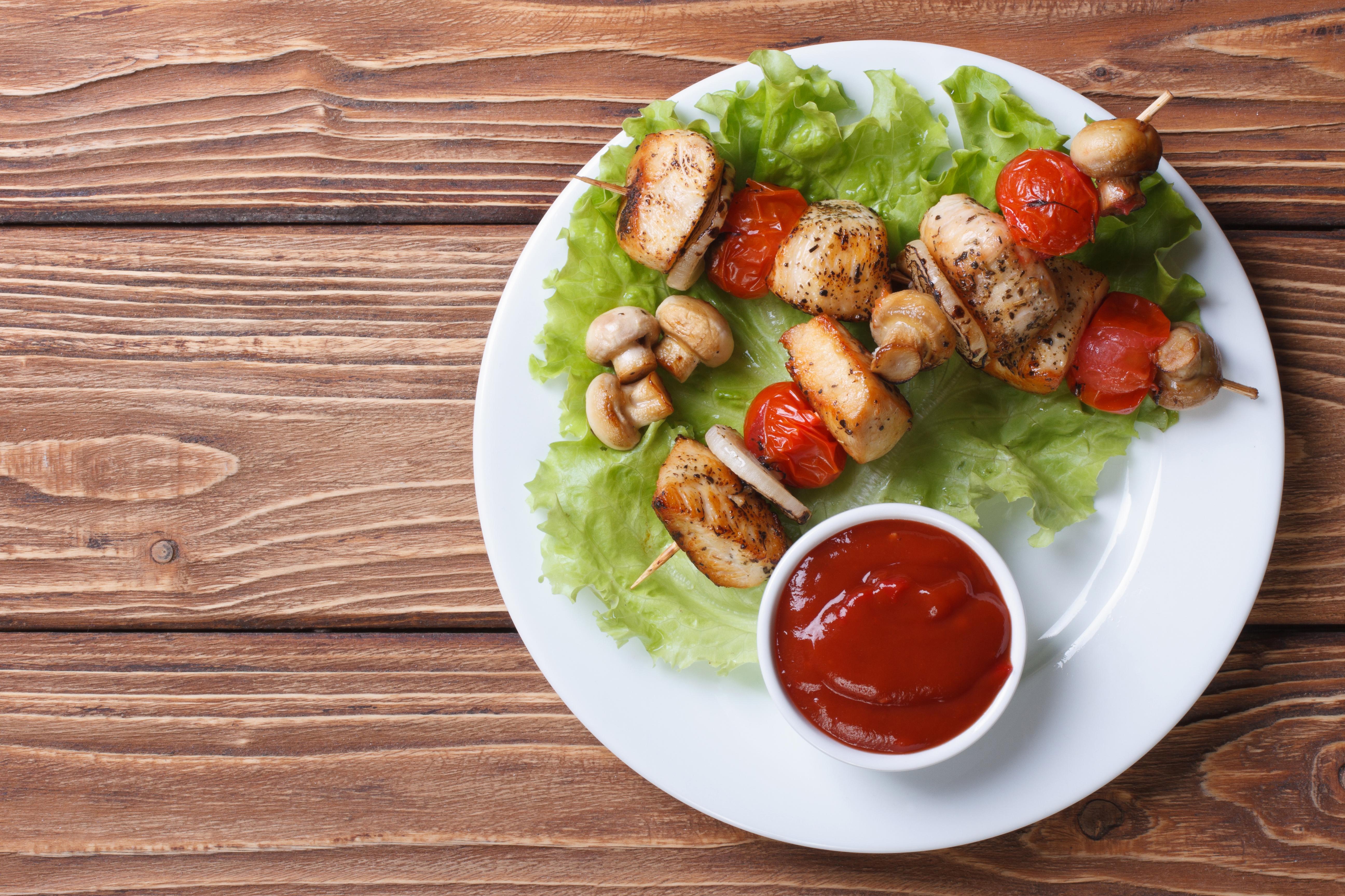 Zwei Grillspieße mit Fleisch und Gemüse samt Dip sind auf einem Teller angerichtet.