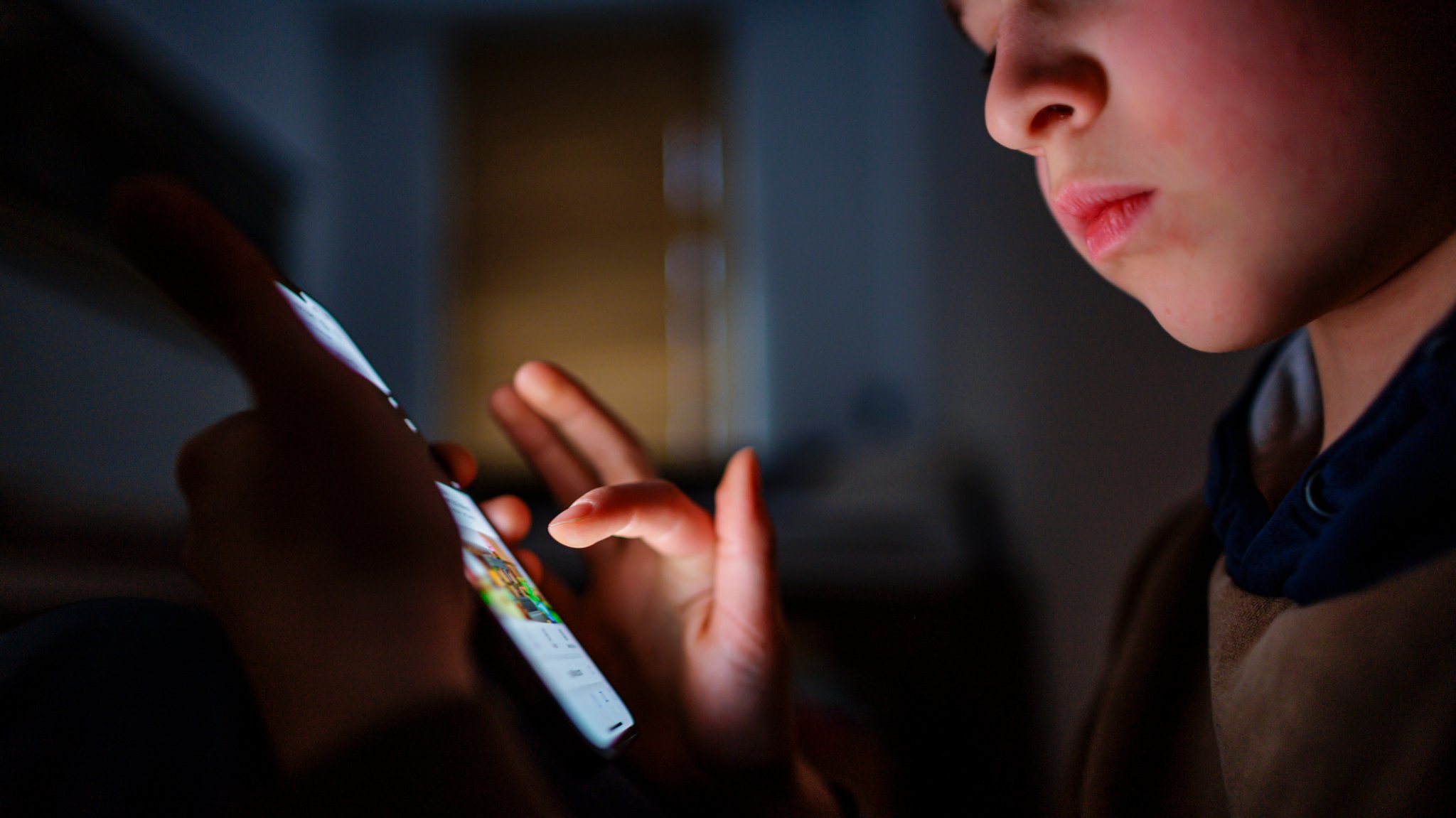 Gestellte Aufnahme zum Thema Kinder nutzen Social Media: Ein Junge sitzt in einem dunklen Raum und wird von einem Smartphone beleuchtet. | Bild: picture alliance / photothek.de | Thomas Trutschel Gestellte Aufnahme zum Thema Kinder nutzen Social Media: Ein Junge sitzt in einem dunklen Raum und wird von einem Smartphone beleuchtet.