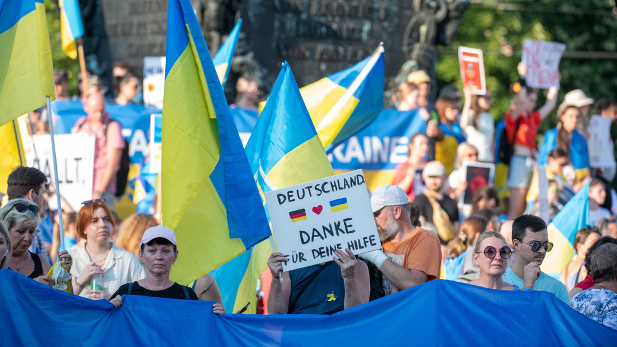 Menschen bei einer Demonstration mit gelb-blauen Flaggen und einem Schild "Deutschland Danke für Deine Hilfe"