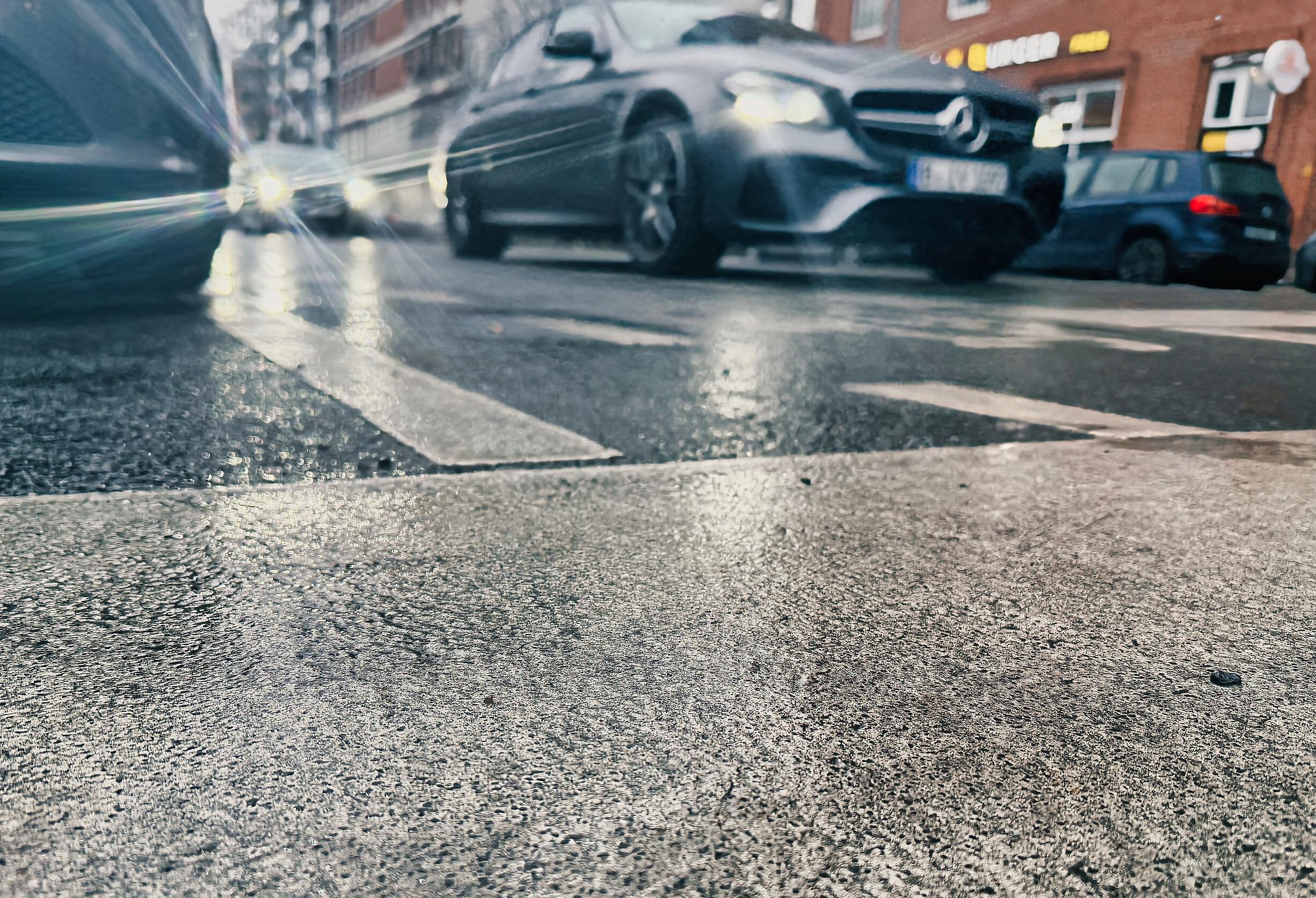 Eine Straße überzogen mit Blitzeis. Im Hintergrund Autos