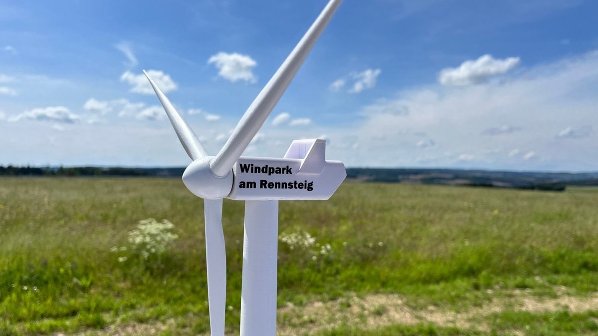 Ein kleines Windrad steht bei einer Wiese. "Windpark am Rennsteig" steht auf dem Windrad. 