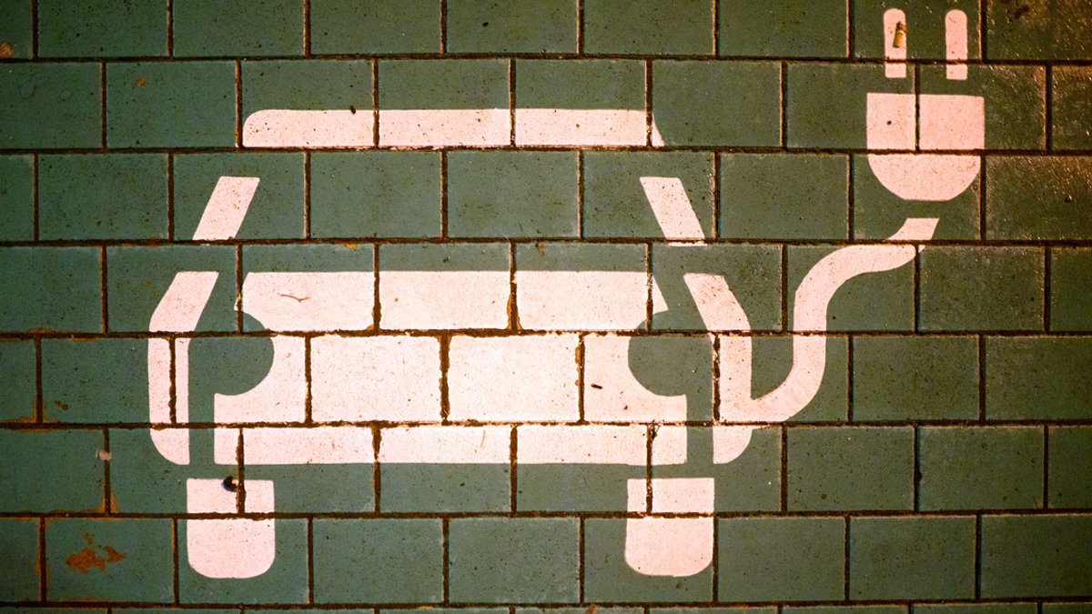 Ein Symbol markiert einen Parkplatz mit einer öffentlichen Ladesäule für Elektroautos an einem Einkaufszentrum.