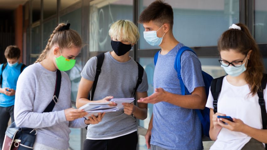 Schülerinnen und Schüler mit Masken im Gesicht und Heften in der Hand (Symbolbild)