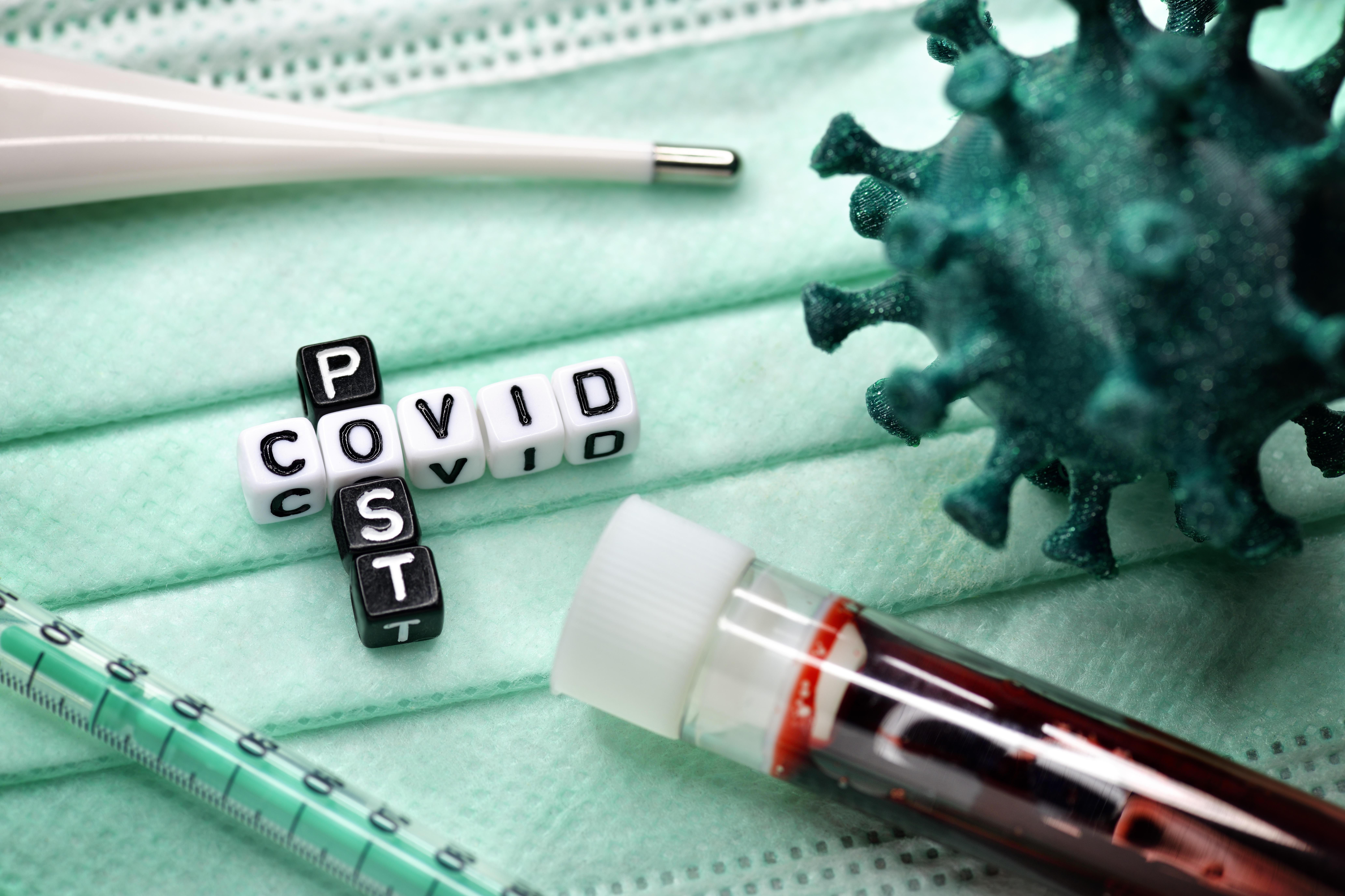 Buchstabenwürfel bilden den Schriftzug Post Covid neben Blutprobe und Coronavirus-Modell