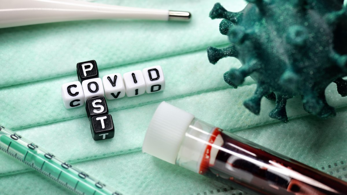 Buchstabenwürfel bilden den Schriftzug Post Covid neben Blutprobe und Coronavirus-Modell