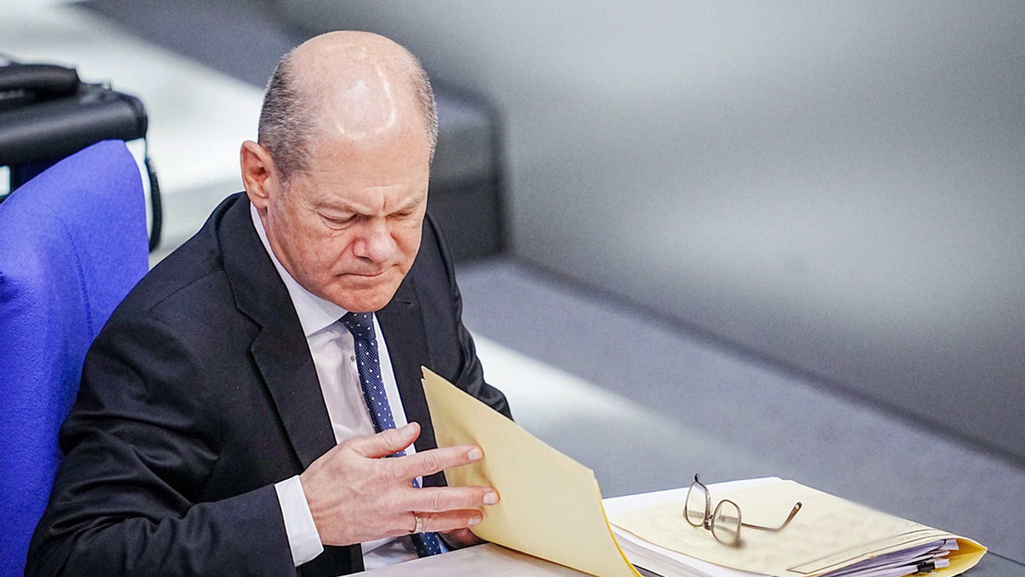 Bundeskanzler Olaf Scholz (SPD) blättert an seinem Platz im Bundestag in Unterlagen.