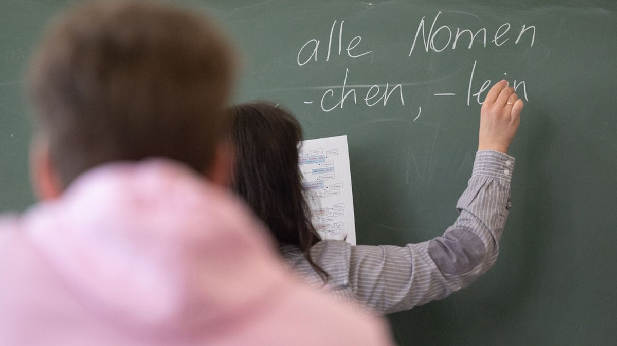 Eine Lehrerin schreibt etwas an die Tafel im Klassenzimmer. (Symbolbild)