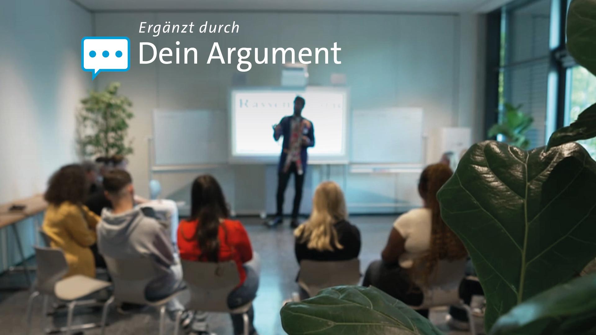 Respekt Coach vor Gruppe in Raum; Bildungsprojekte wie die Respekt Coaches könnten aufgrund von Kürzungen und Umstrukturierungen im Familienministerium gefährdet sein und möglicherweise nicht mehr finanziell unterstützt werden.