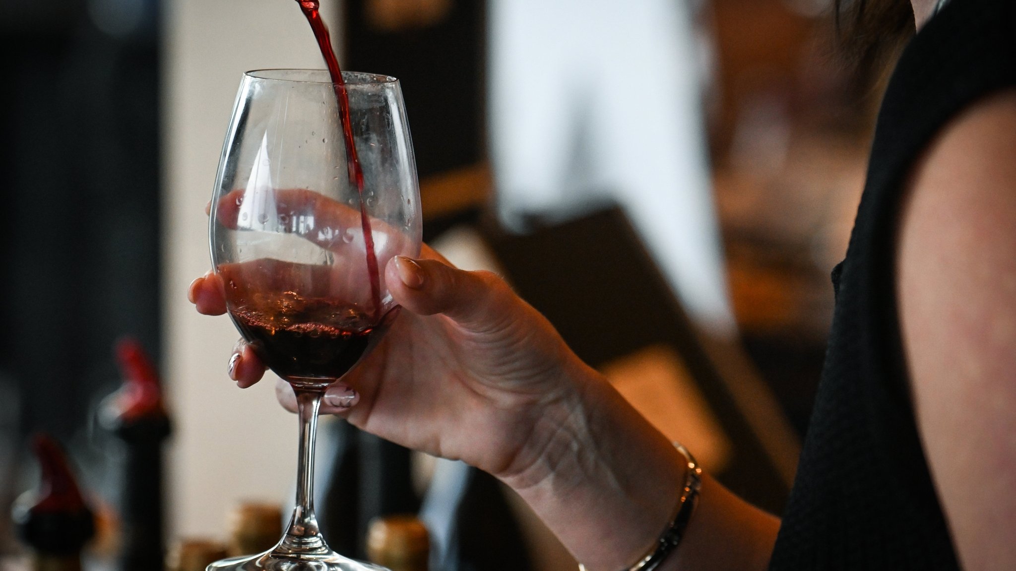 Einer Frau wird ein Glas Rotwein eingeschenkt. Laut einem Positionspapier der DGE sind auch geringe Mengen Alkohol schädlich. Die DGE rät daher, ganz auf Alkohol zu verzichten.